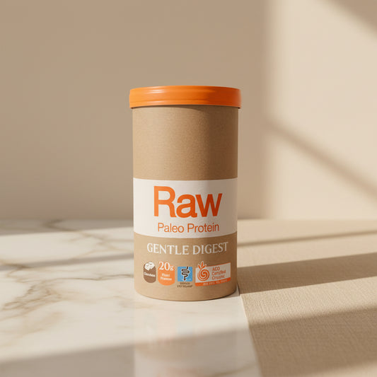 A brown cardboard tub of Raw Paleo Protein Gentle Digest powder with an orange lid, sitting on a light countertop against a white tiled wall.